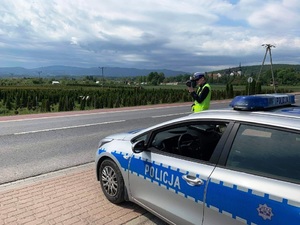 Radiowóz stoi przy drodze, obok policjant z laserowym miernikiem prędkości.