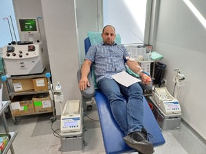 Osoba siedzi na fotelu i oddaje krew. Przy fotelu stoją urządzenia do pobierania krwi.
