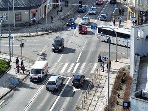 Skrzyżowanie dróg po którym poruszają się pojazdy i piesi widziane z góry.