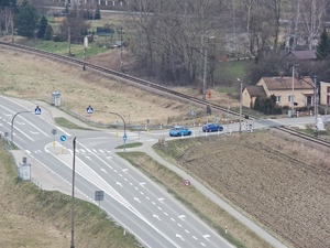 Skrzyżowanie drogi z przejazdem kolejowym na którym stoją samochody.