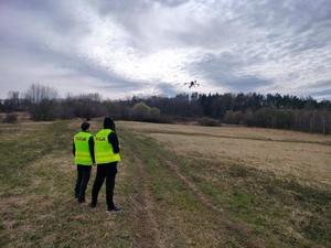 Policjanci na trawiastej łące z dronem który jest w powietrzu.