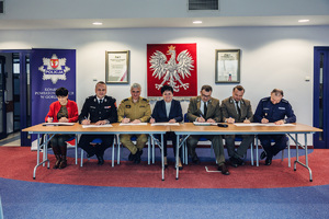 Siedem osób, przedstawicieli służb i instytucji powiatu gorlickiego podpisuje siedząc przy stole w auli apel do mieszkańców powiatu.