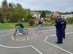 Policjant obserwuje przejazd na rowerze przez tor przeszkód jednego z uczestników turnieju.