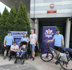 Policjanci razem z małym chłopcem, który siedzi na wózku stoją z rowerami przed Komendą Powiatową Policji w Gorlicach.