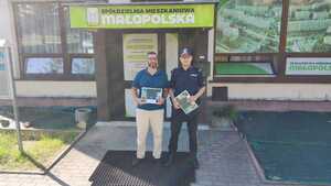 Policjant stoi przed wejściem do budynku spółdzielni mieszkaniowej.