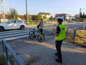 Policjantka daje odblask chłopcu, który przeszedł przez przejście dla pieszych z rowerem.