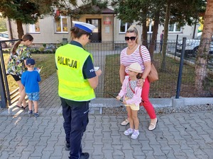 Policjantka daje odblask dziecku, które z rodzicem idzie do przedszkola.