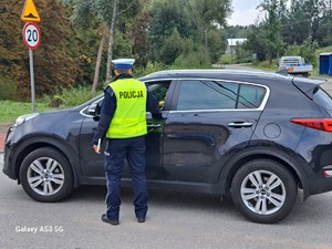 Policjant stoi obok samochodu osobowego i kontroluje trzeźwość kierowcy.