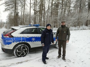 Policjant i strażnik leśny stoją przed radiowozem.