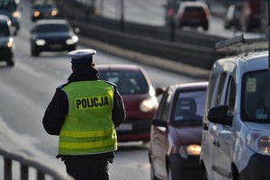 Policjant stoi na poboczu drogi i obserwuje jadące samochody.