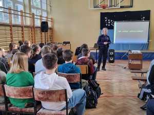 Policjantka na sali gimnastycznej prowadzi prelekcję na temat cyberprzemocy. na tablicy wyświetlana jest prezentacja.