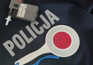 Na mundurze z napisem Policja, leży policyjny lizak i urządzenie do badania zawartości alkoholu w wydychanym powietrzu.