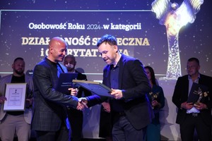 Laureat otrzymuje od prowadzącego galę wyróżnienie. Z tyłu na scenie stoją inny wyróżnieni.