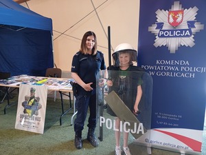 Policjantka z chłopcem ubranym w zestaw ochronny policjanta przy stoisku policji.