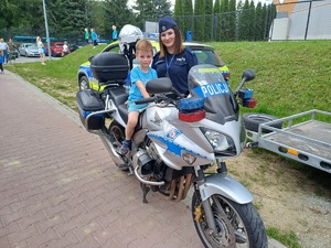 Dziecko siedzi na motocyklu policyjnym, obok stoi policjantka.