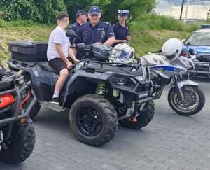 Policjanci stoją przy quadzie i motocyklu. Na policyjnym quadzie siedzi chłopiec.