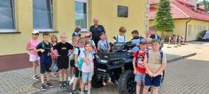 Policjant z quadem stoi razem z dziećmi obok szkoły.