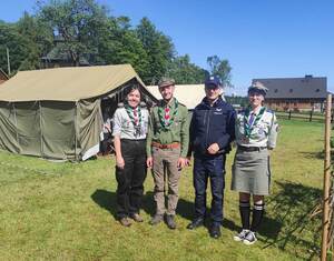 Policjant i trójka harcerzy. W tle namiot harcerski.