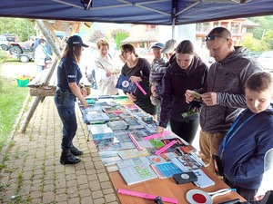 Policjantka rozdaje  ulotki informacyjne i materiały profilaktyczne stojącym przy policyjnym stoisku kilku osobom