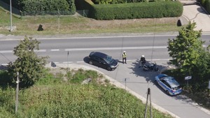 Policjant kontroluje na drodze motocyklistę. Obok stoi policyjny raiowóz.