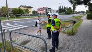 Dwóch policjantów stojących na chodniku i dziecko przechodzące przez przejście dla pieszych.