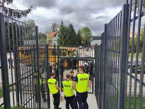 Kilku policjantów stoi w ogrodzonym siatką przejściu prowadzącym na stadion.