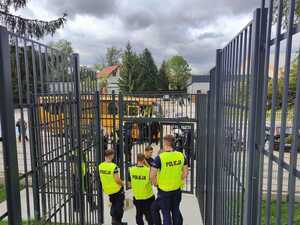 Kilku policjantów stoi w ogrodzonym siatką przejściu prowadzącym na stadion.