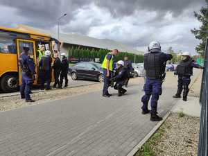 Policjanci wyprowadzają z autobusu osoby, kontrolują je i wprowadzają  na stadion.