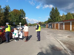 Policjanci wraz z dziećmi na ulicy rozmawiają z kierowcą zatrzymanego pojazdu.