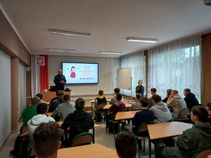 Policjant w trakcie prelekcji dla siedzących w ławkach uczniów.