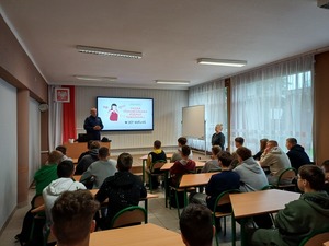 Policjant w trakcie prelekcji dla siedzących w ławkach uczniów.