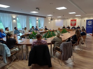 Przy stole siedzą policjanci. Na przeciw na sali wokół stołu siedzą uczestnicy debaty.