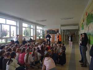 Dzieci siedzą na sali i słuchają prelekcji stojącego przed nimi Policjanta.