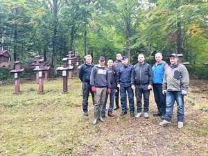 Grupa osób stoi obok krzyży na cmentarzu w lesie.