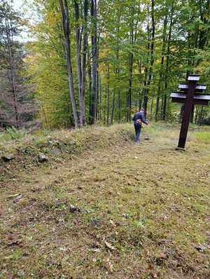 Osoba kosi trawę na cmentarzu w lesie.