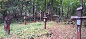 Dwie osoby koszą trawę pomiędzy drewnianymi krzyżami w lesie.