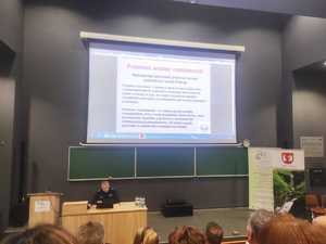 Policjant prowadzi prelekcję dla uczestników konferencji. Wyświetlany jest slajd z prezentacji.