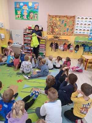 Policjantka pokazuje dzieciom w sali kamizelkę odblaskową.