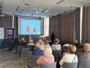 Policjant omawia siedzącym na krzesłach osobom wyświetlony slajd.