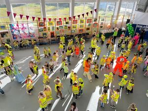 Dzieci w kamizelkach odblaskowych bawią się na sali.