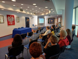 Osoby siedzą na auli i słuchają wykładu policjanta.