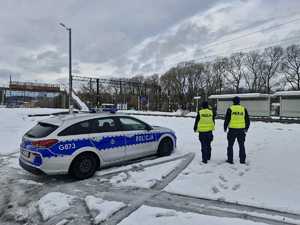 Dwóch policjantów obok radiowozu obserwuje rejon stacji kolejowej.