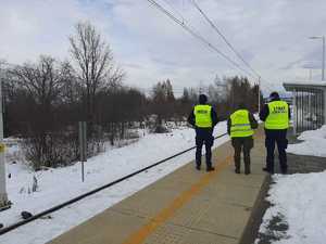 Policjant żołnierz i pracownik służby ochrony kolei stoją na peronie stacji kolejowej.