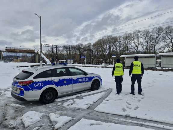 Dwóch policjantów obok radiowozu obserwuje rejon stacji kolejowej.