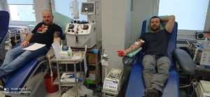 Dwóch mężczyzn siedzi na fotelach i oddaje krew. Obok foteli stoją aparaty pobierające krew.