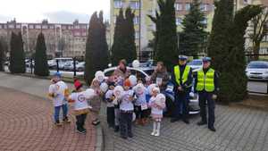 Dwóch policjantów razem z dziećmi stoi obok radiowozu.
