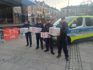 Czterech policjantów stoi obok radiowozu i trzyma w rękach paczki z napisem szlachetna paczka.