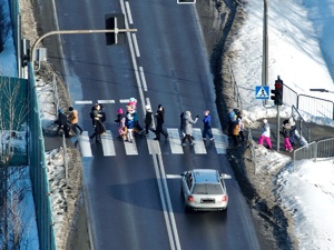 Grupa dzieci przechodzi przez przejście dla pieszych. Przed przejściem stoi samochód.