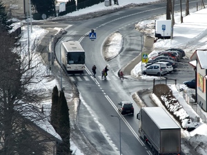 Kilka osób przechodzi przez przejście dla pieszych. Przed przejściem stoją pojazdy.