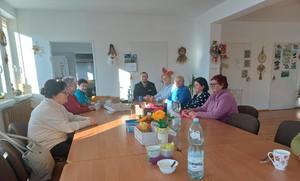 Policjant siedzi przy stole razem z seniorami.